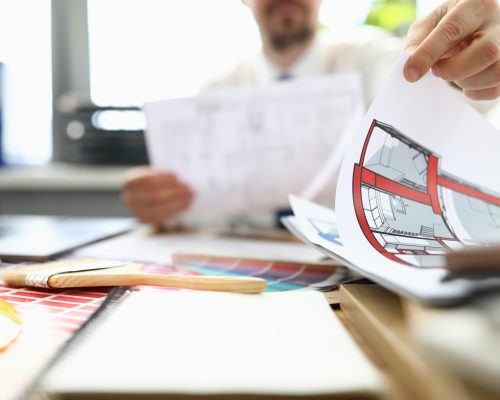 Male designer sits at table and looks at floor plan. Interesting design home. Use two primary colors in interior. Choice colors for decoration. Find right color scheme. Home source positive energy