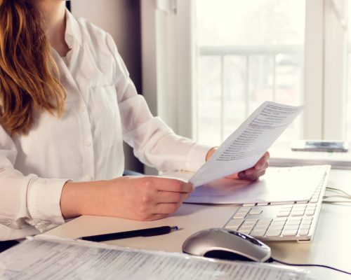 Unrecognizable businesswoman working at desk in the office and reading business reports.